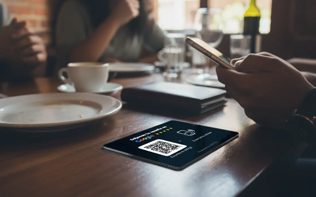 Comensal acercando su celular a la tarjeta negra de reseñas sobre la mesa de un restaurante, junto a la cuenta